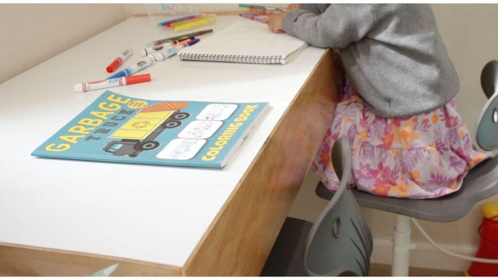 A little girl is drawing on a DIY play desk with markers and crayons