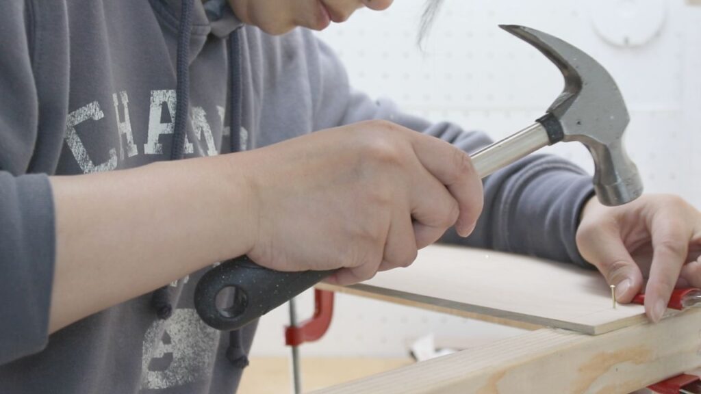 assembling sides onto the DIY whiteboard top play desk with wood glue, nails and a metal hammer