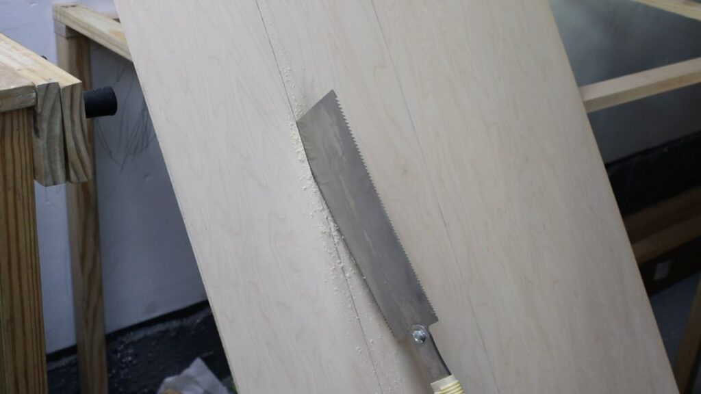 cutting desk sides out of a quarter-inch plywood board with a pull saw for the DIY whiteboard top play desk